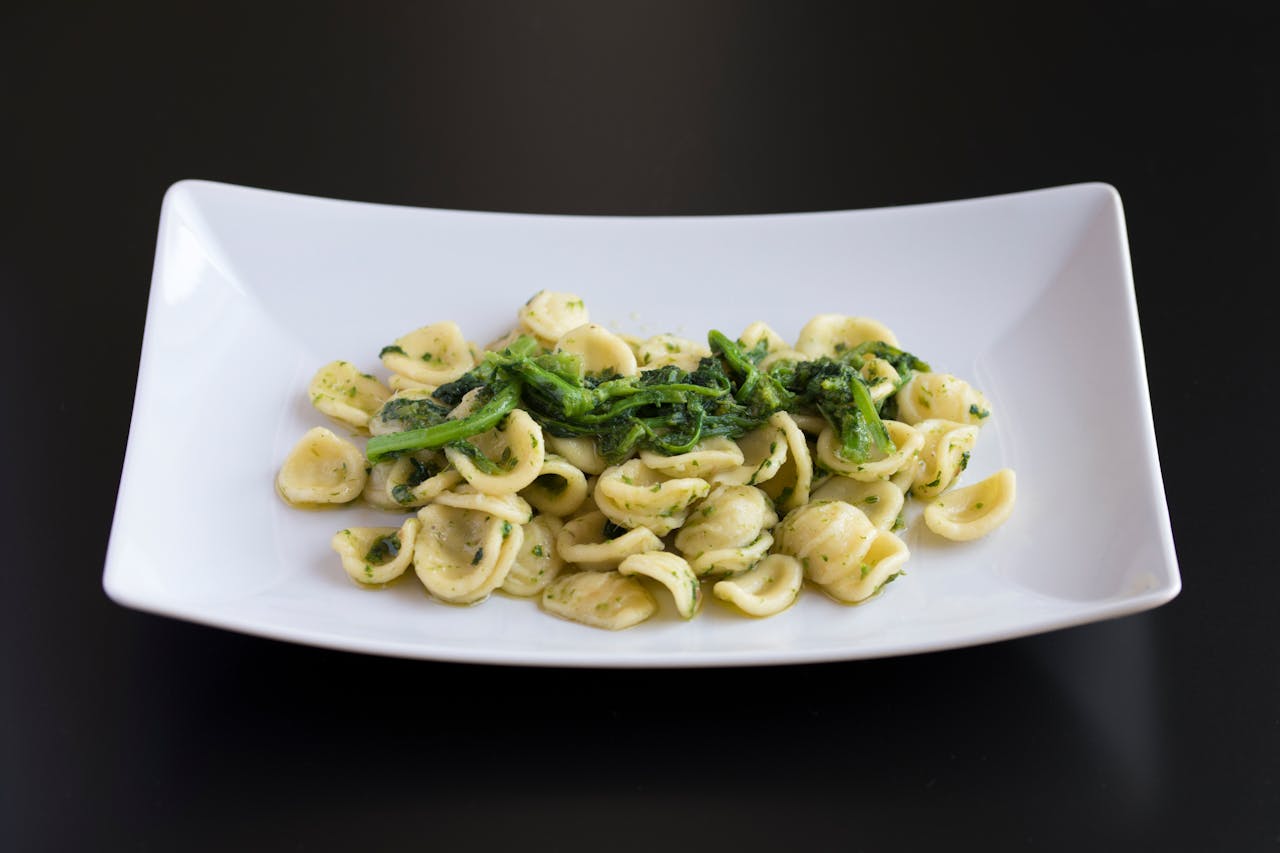 about-us Close-up of orecchiette pasta with greens elegantly plated, showcasing vibrant colors and delicious presentation.